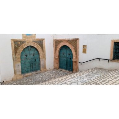 Deux portes colorées en bois dans un mur en pierre, avec des escaliers en pavés.